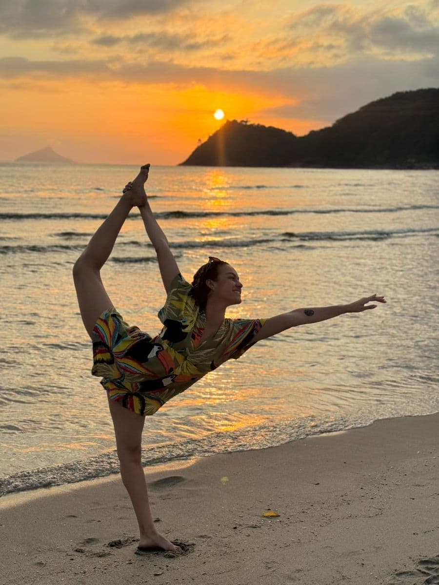 Melissa Oliveira em pose de dança na praia, ao pôr do sol