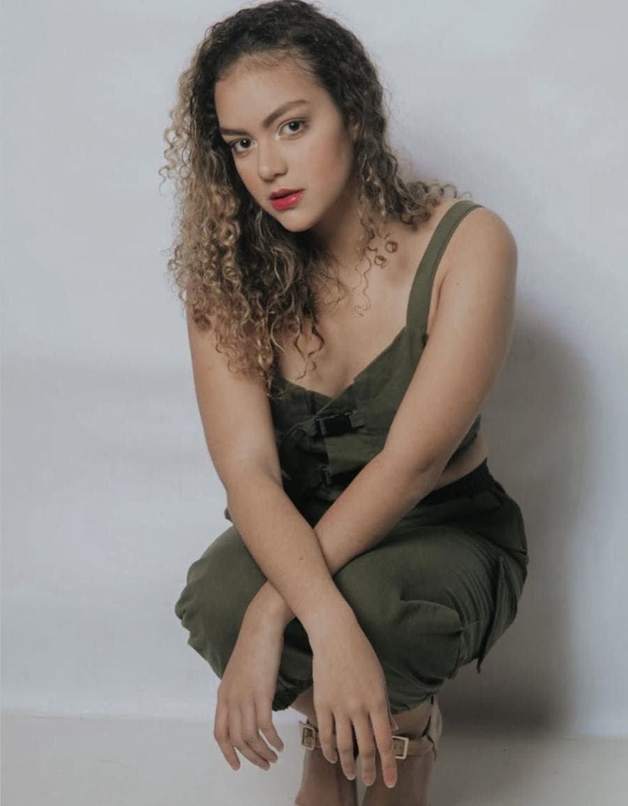 Melissa Oliveira em pose editorial, macacão verde militar, olhar direto para a câmera, fundo neutro